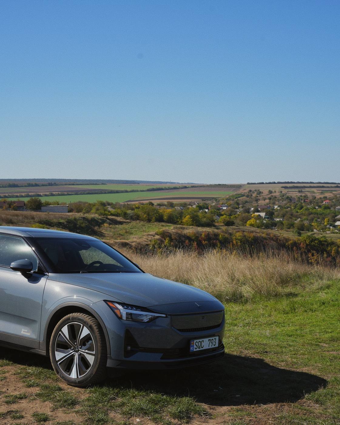 The Polestar 2 at the viewpoint above Furceni, with the village and the fields behind