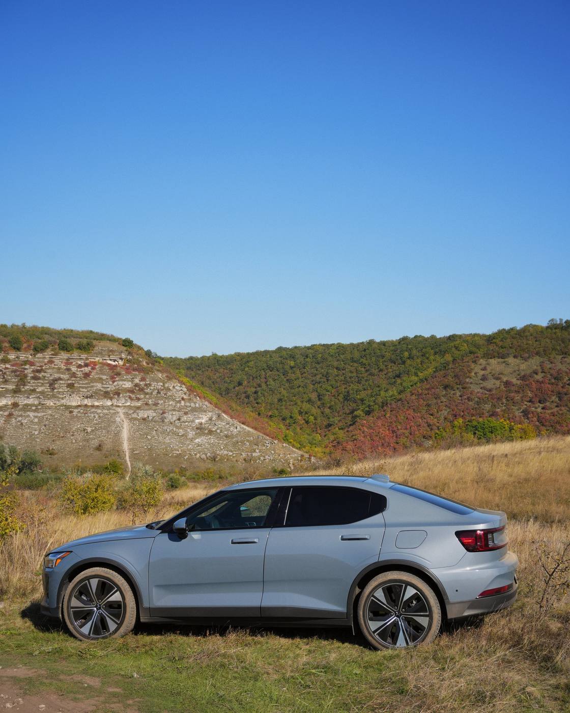 The car in profile on a grassy slope, with the rock bank behind