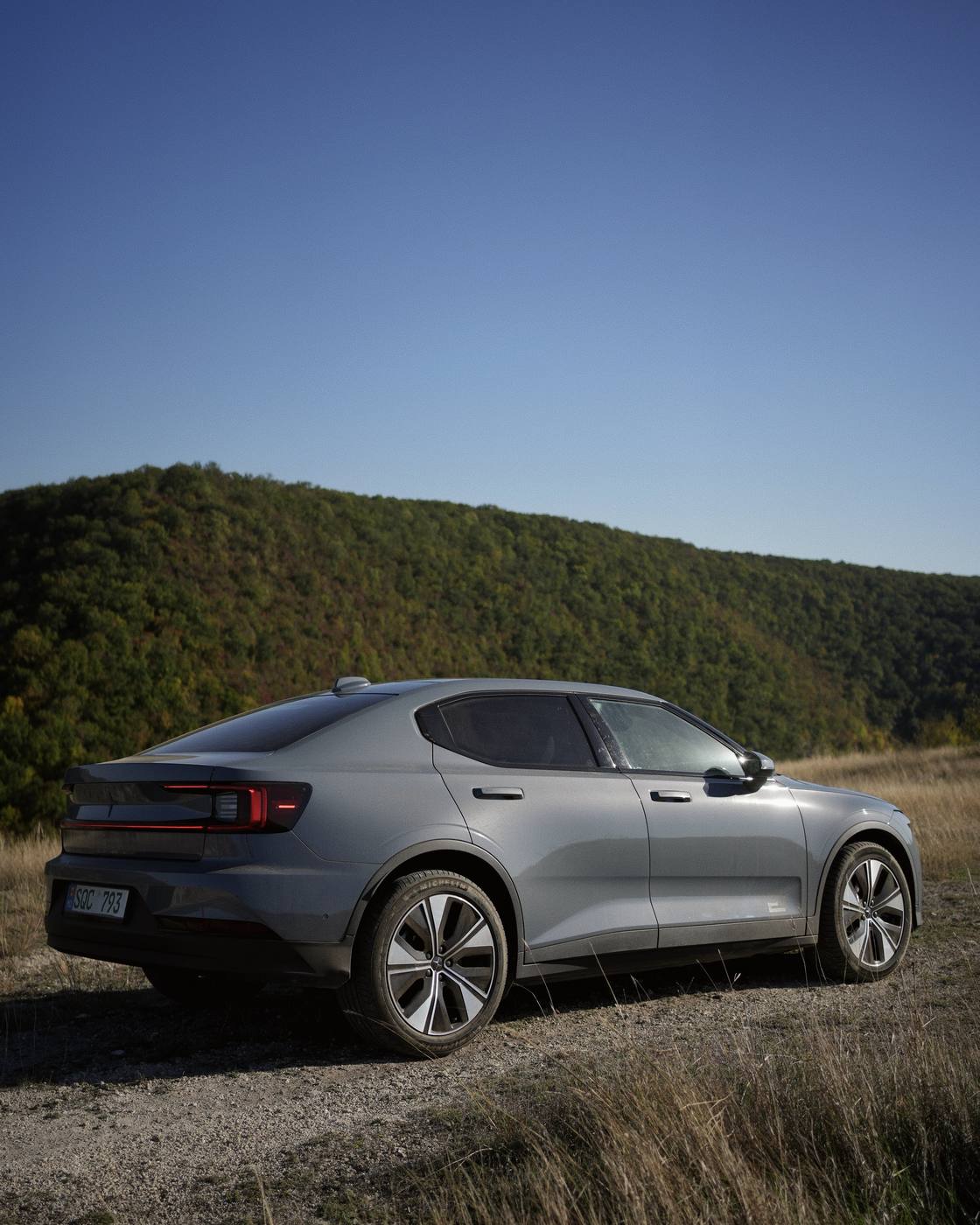 The car from behind, on the gravel track, with the wooded hill behind